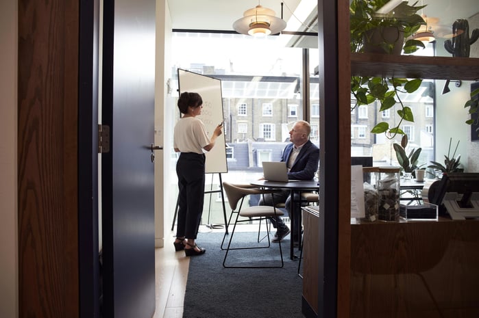 Woman standing and speaking to sitting man in an office setting