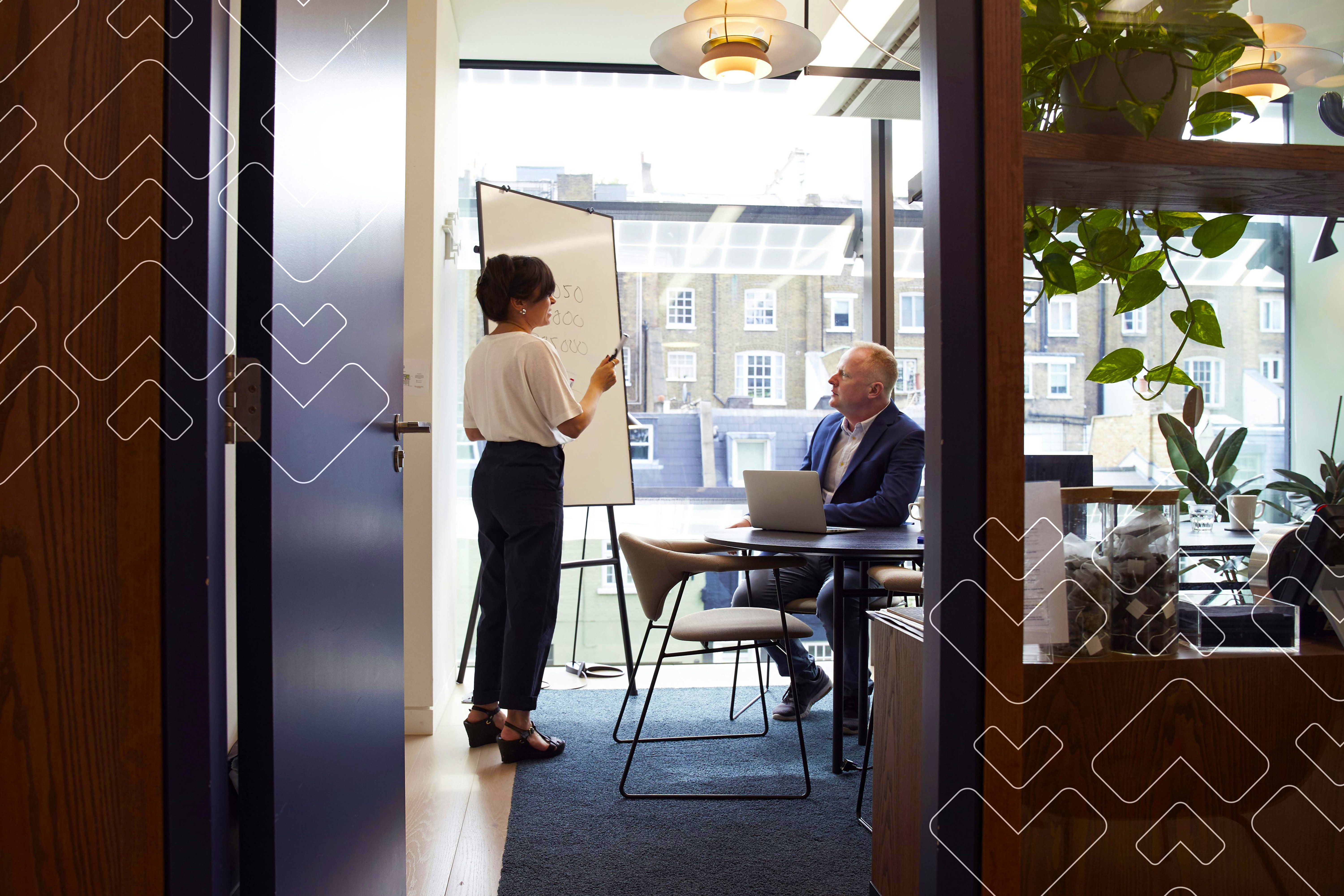 Woman speaking to seated older man at table, with presentation