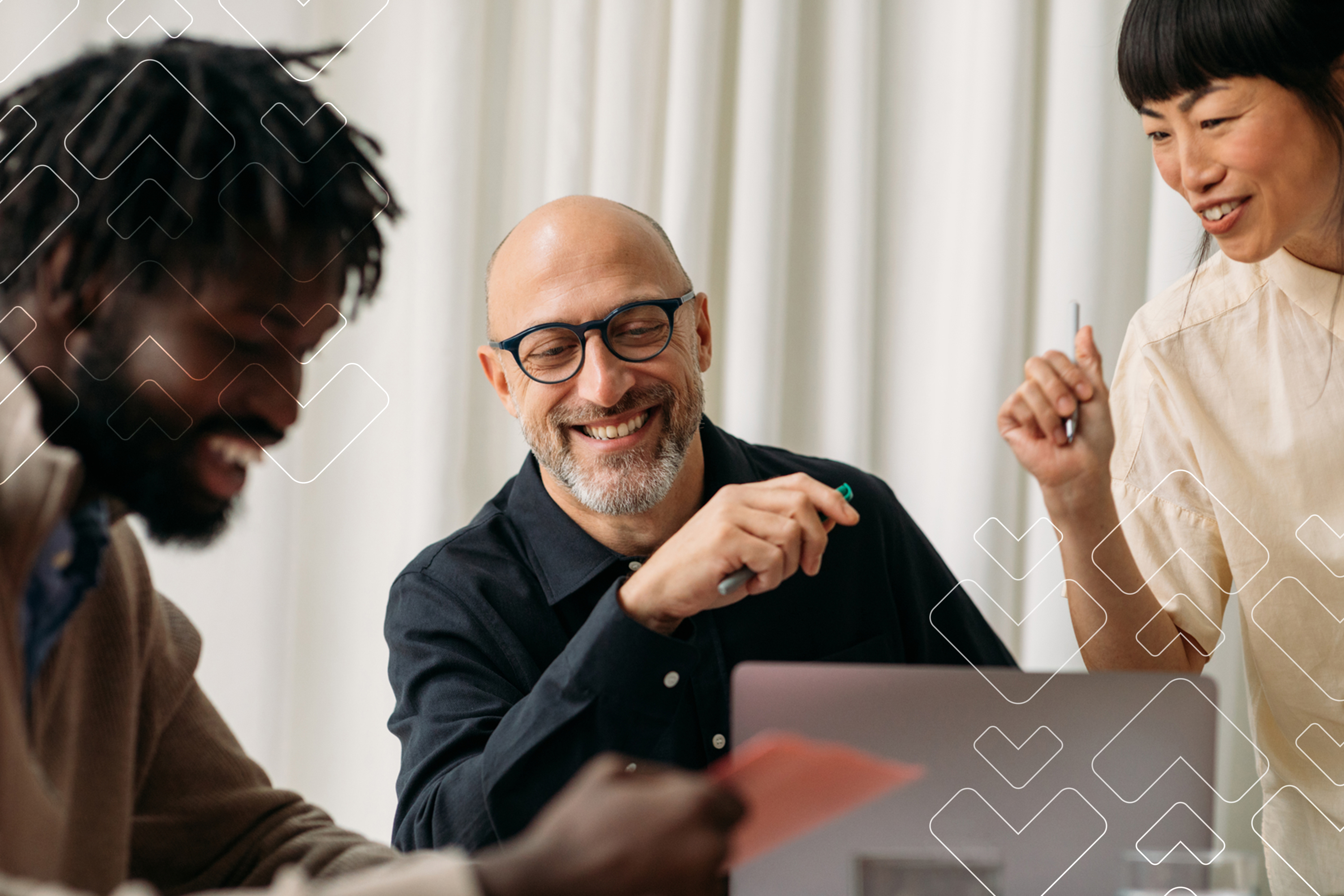 Man sitting at desk with coworkers at desk, all are smiling